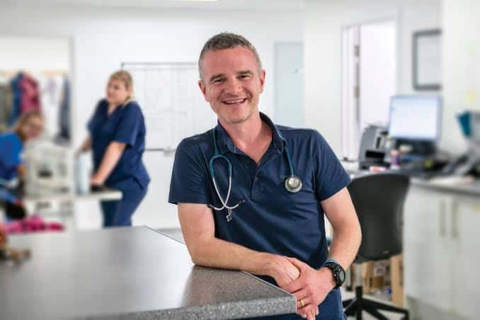 Dave Nicol står i en dyreklinik med stetoskop og kolleger i baggrunden